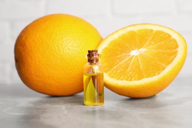 Bottle of essential oil with oranges on grey marble table, closeup