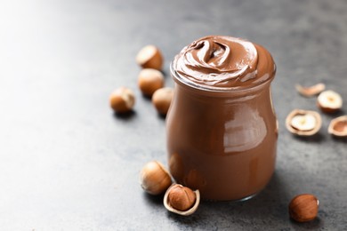 Glass jar with tasty chocolate hazelnut spread and nuts on grey table. Space for text