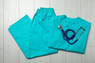 Photo of Clean scrubs and stethoscope on wooden background, top view. Medical objects