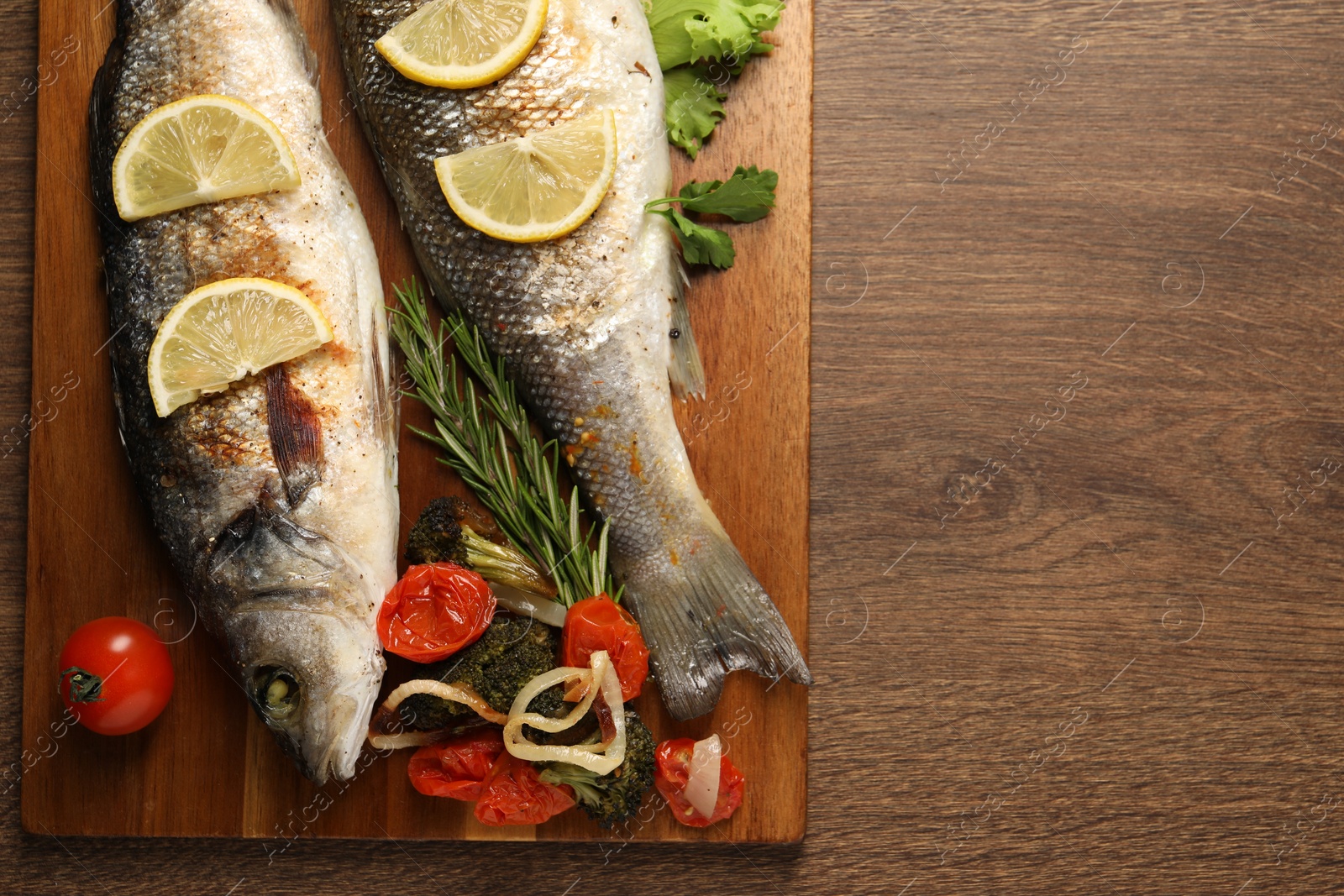 Photo of Delicious baked fish and vegetables on wooden table, top view. Space for text