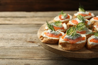 Photo of Tasty canapes with salmon, cucumber, cream cheese and dill on wooden stand, closeup. Space for text