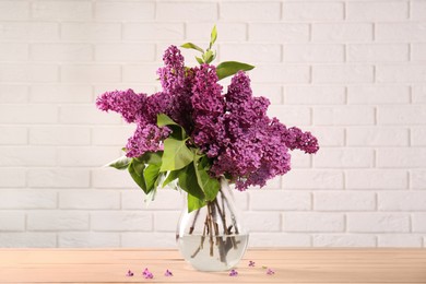 Beautiful lilac flowers in vase on wooden table near white tiled wall