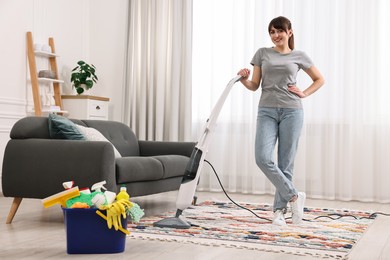 Photo of Happy young housewife vacuuming rug at home