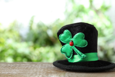 Black leprechaun hat with clover leaf on wooden table, space for text. St Patrick's Day celebration