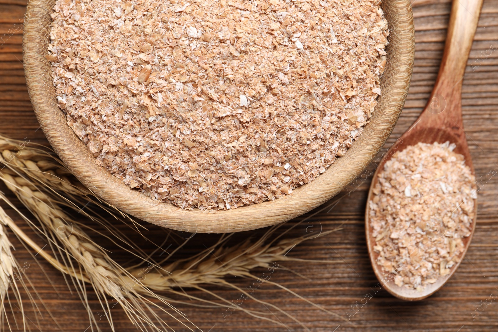 Photo of Spoon and bowl with wheat bran on wooden table, flat lay