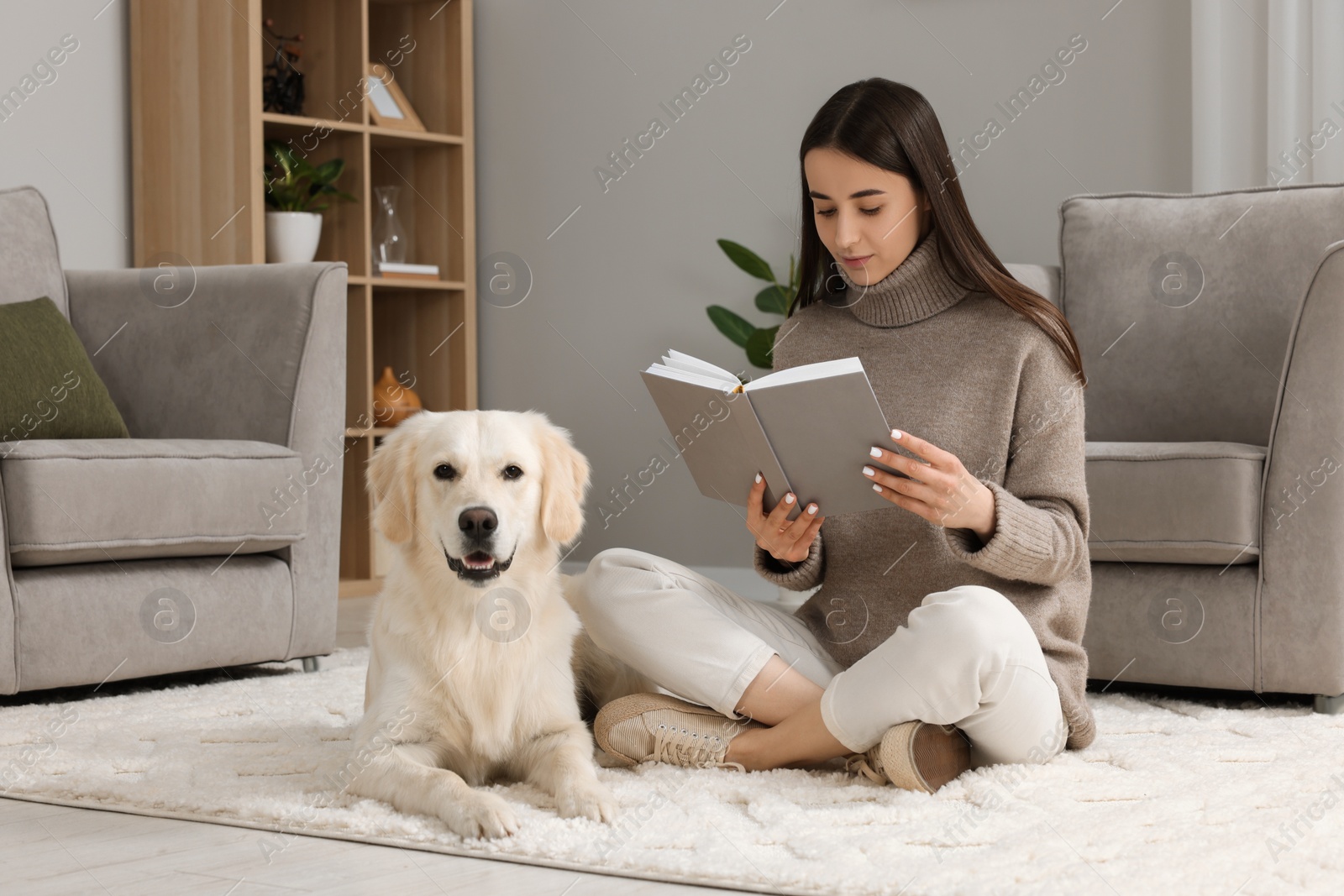 Photo of Woman reading book with cute Labrador Retriever dog on floor at home. Adorable pet