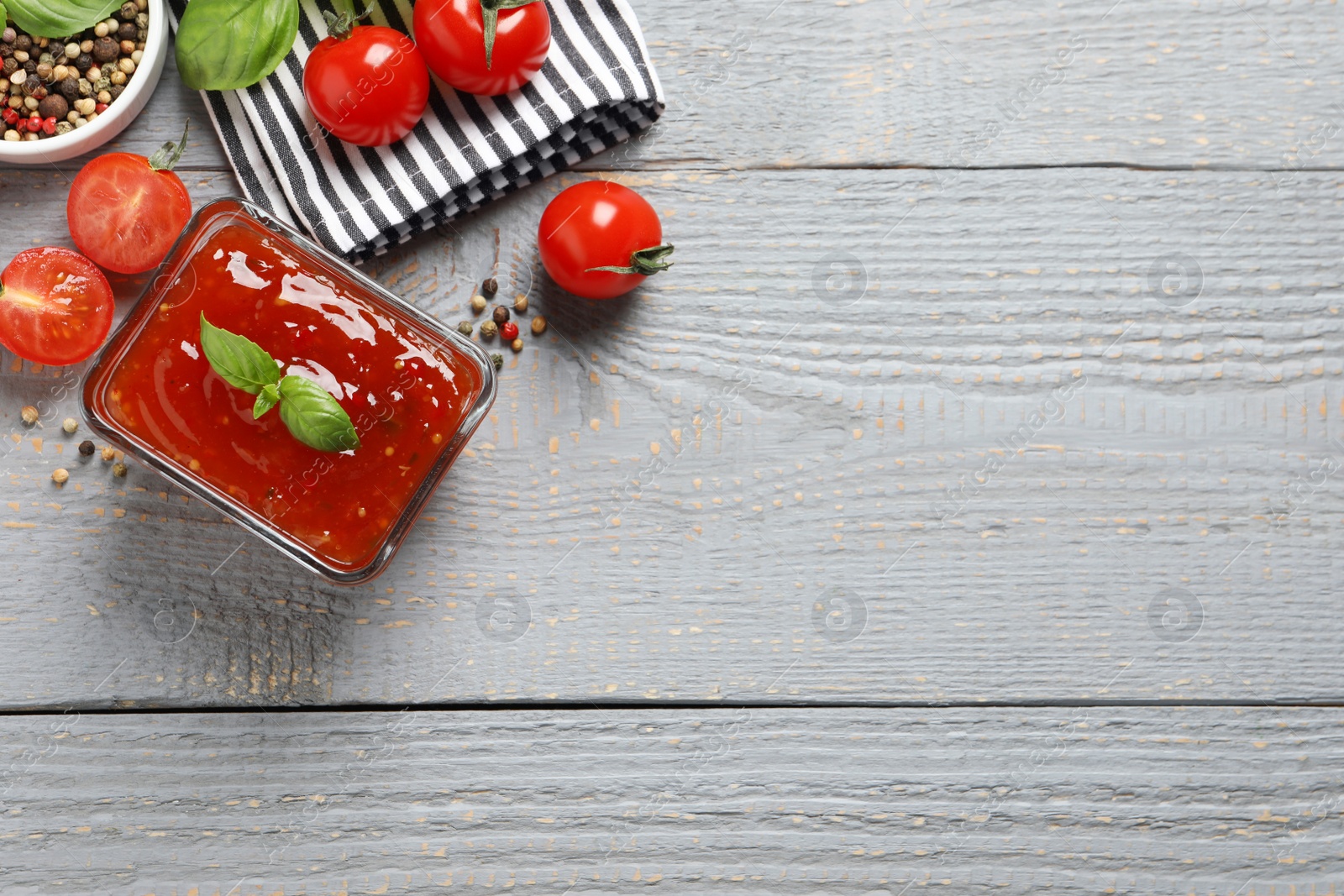 Photo of Spicy chili sauce and ingredients on grey wooden table, flat lay. Space for text