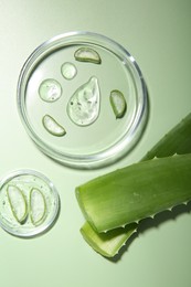 Photo of Cut aloe vera and drops of cosmetic gel on light green background, flat lay