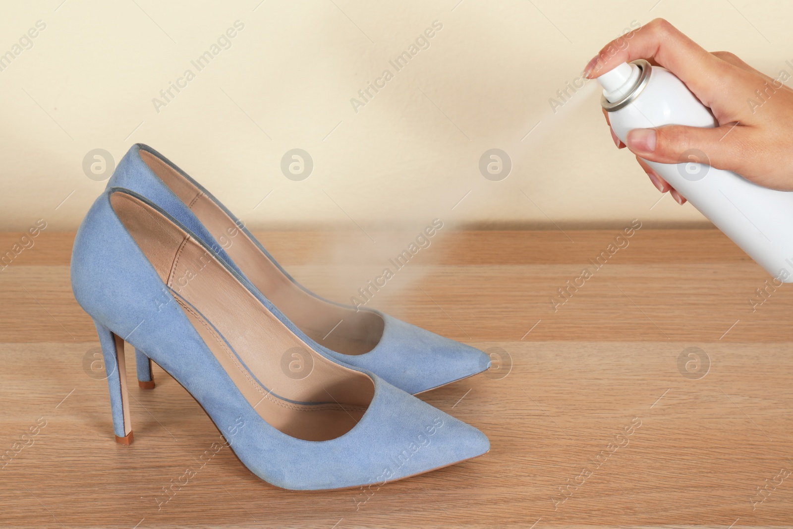 Image of Woman spraying deodorant over pair of shoes at home, closeup