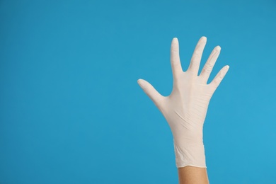 Photo of Doctor wearing medical gloves on light blue background, closeup. Space for text