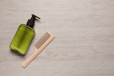 Bottle of shampoo and hairbrush on white wooden table, flat lay. Space for text