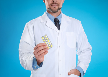 Professional pharmacist with pills on light blue background, closeup