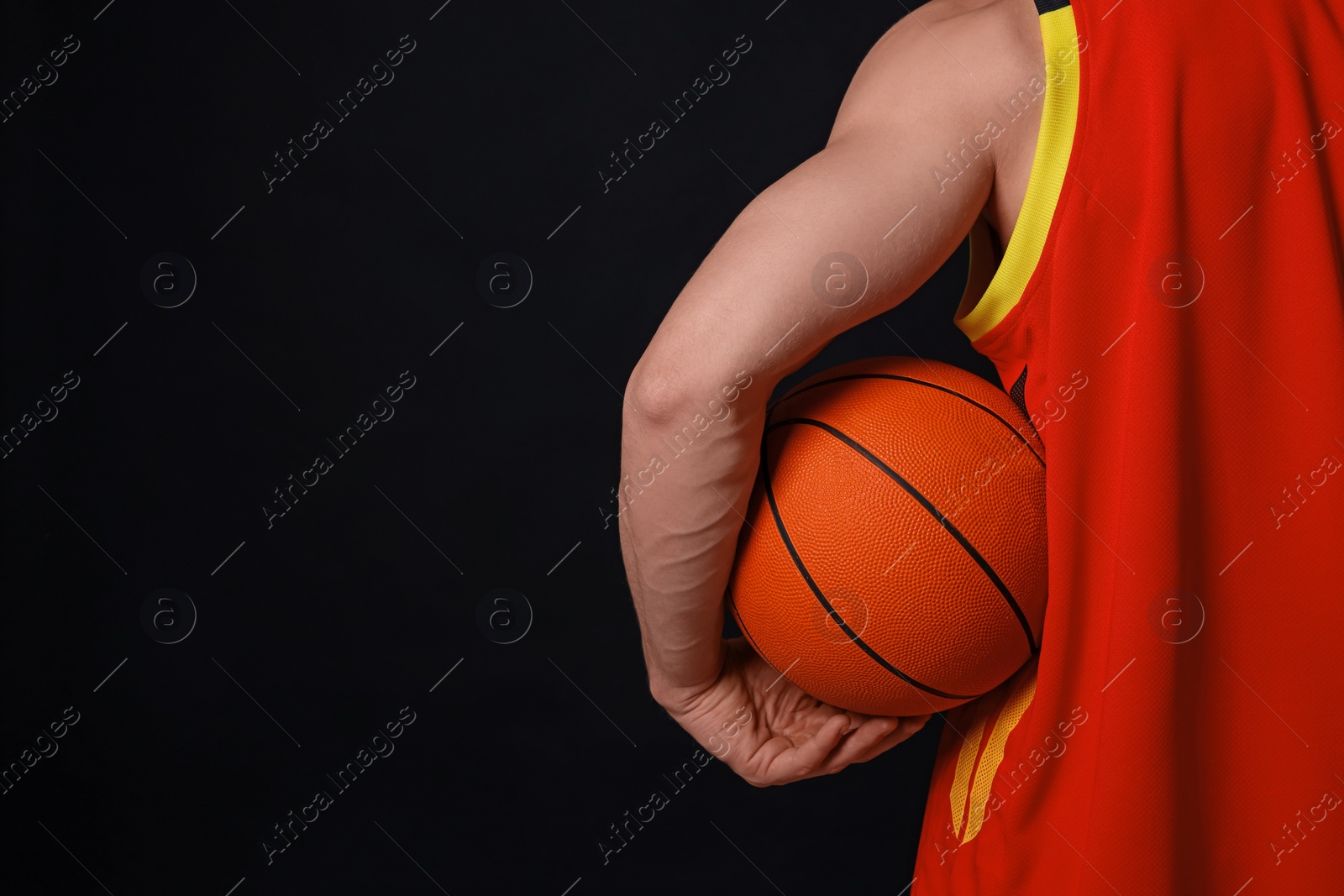 Photo of Athletic man with basketball ball on black background, closeup. Space for text