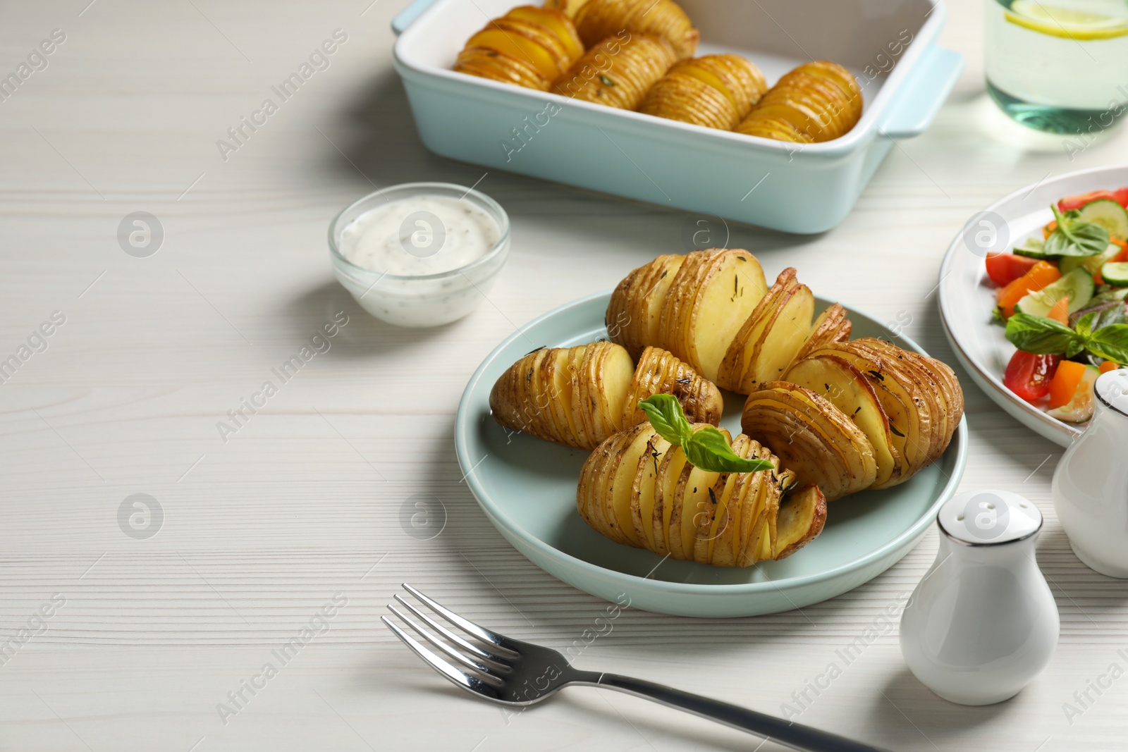 Photo of Delicious homemade Hasselback potatoes served on white wooden table. Space for text