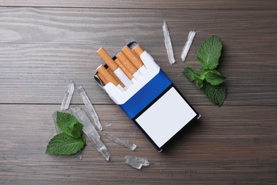 Photo of Pack of cigarettes, menthol crystals and mint on wooden table, flat lay