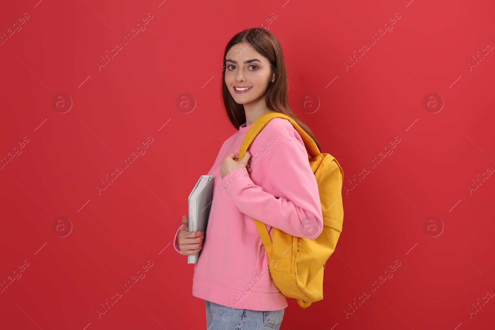 Photo of Teenage student with backpack and book on red background