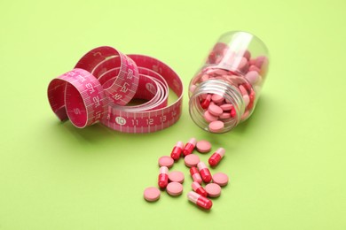 Photo of Jar of weight loss pills and measuring tape on green background