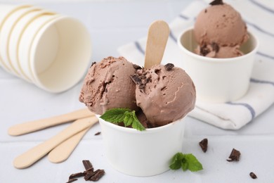 Photo of Paper cups with tasty chocolate ice cream on white tiled table, closeup