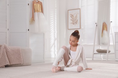 Photo of Little ballerina stretching on floor at home. Space for text