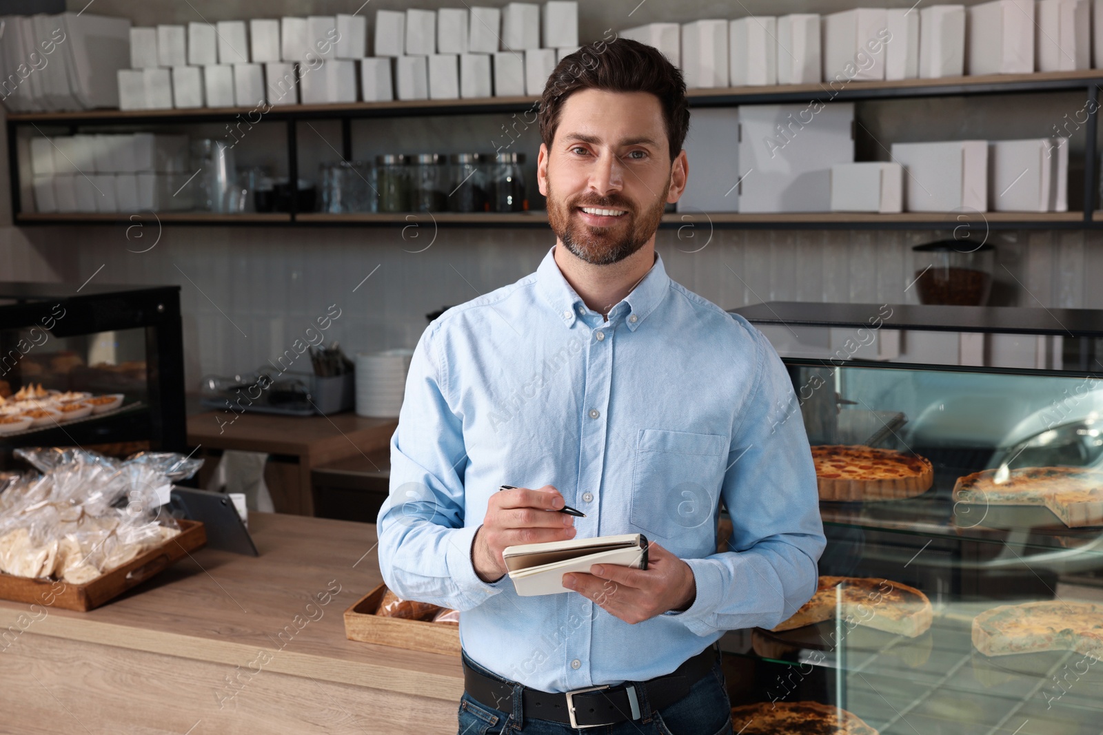 Photo of Happy business owner with notebook and pen in bakery shop