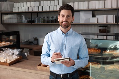 Happy business owner with notebook and pen in bakery shop