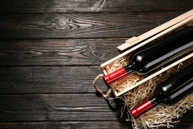 Crate and bottles of wine on wooden table, flat lay. Space for text