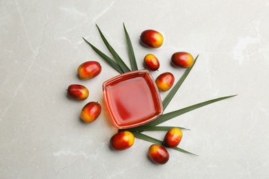 Image of Palm oil in glass bowl, tropical leaf and fruits on light table, flat lay