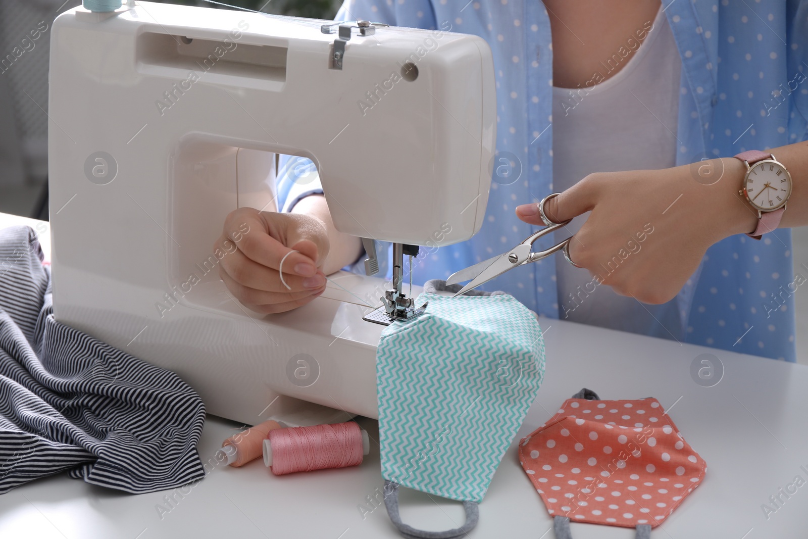 Photo of Woman making cloth mask with sewing machine at white table, closeup