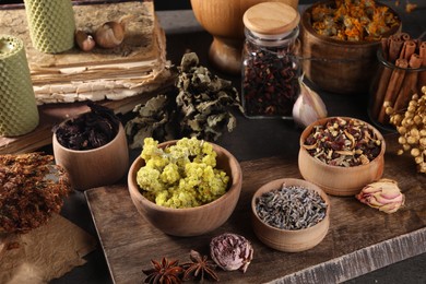 Many different dry herbs, flowers and spices on dark grey table