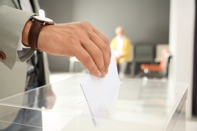 Man putting ballot paper into box at polling station, closeup