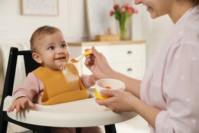 Photo of Mother feeding her little baby at home. Kid wearing silicone bib