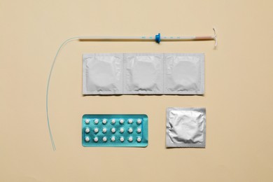 Photo of Contraception choice. Pills, condoms and intrauterine device on beige background, flat lay