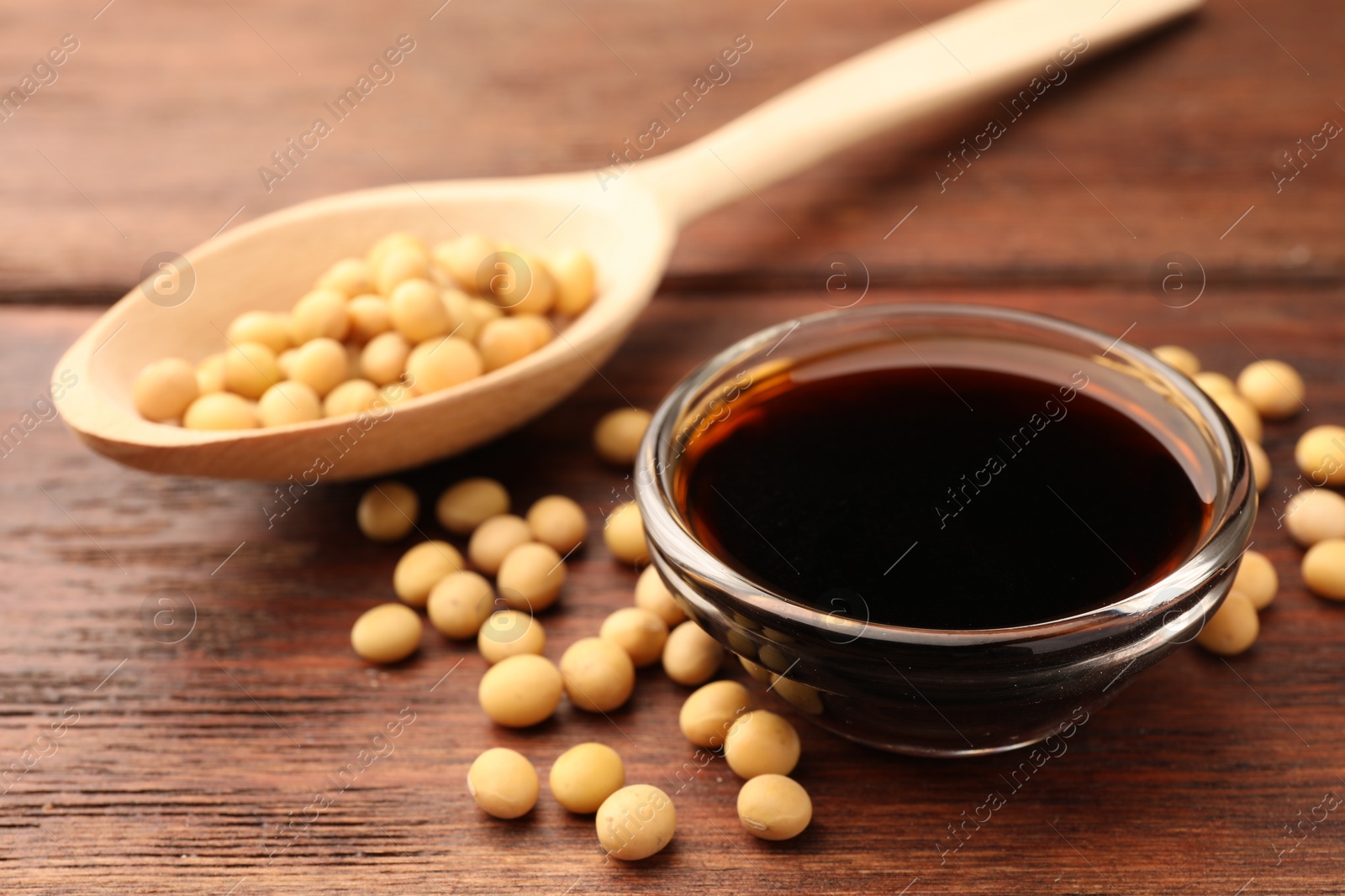 Photo of Soy sauce in bowl and soybeans on wooden table, closeup