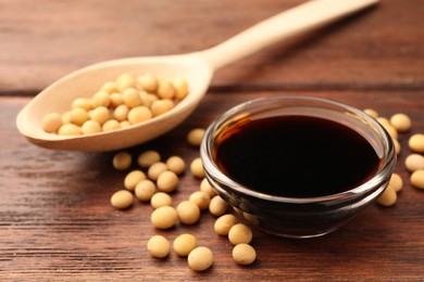 Soy sauce in bowl and soybeans on wooden table, closeup