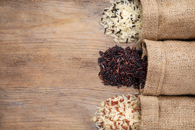 Photo of Overturned bags with brown and polished rice on wooden table, flat lay. Space for text