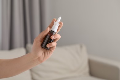 Woman holding nasal spray bottle indoors, closeup. Space for text