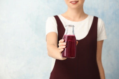 Woman holding bottle of beet smoothie on light background with space for text, closeup