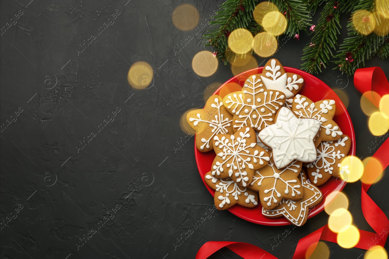 Photo of Tasty Christmas cookies with icing, fir tree branches and ribbon on black table, flat lay. Space for text