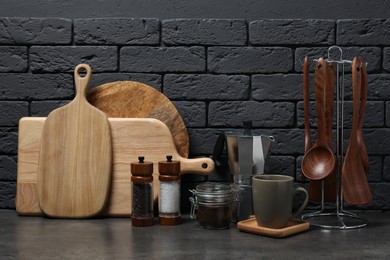 Photo of Wooden cutting boards, utensils, moka pot and cup on gray table near dark brick wall