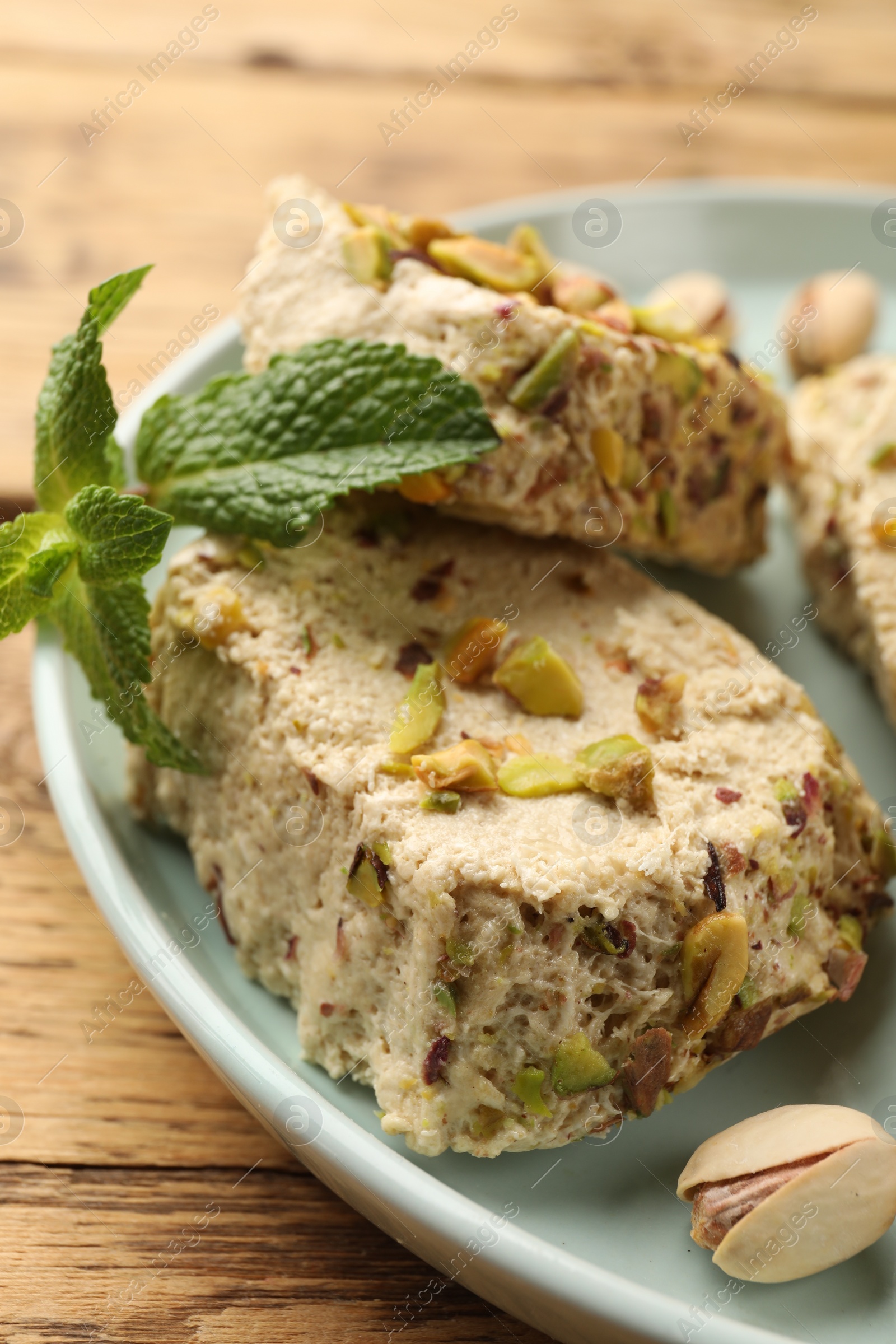 Photo of Tasty halva with pistachios and mint on wooden table, closeup