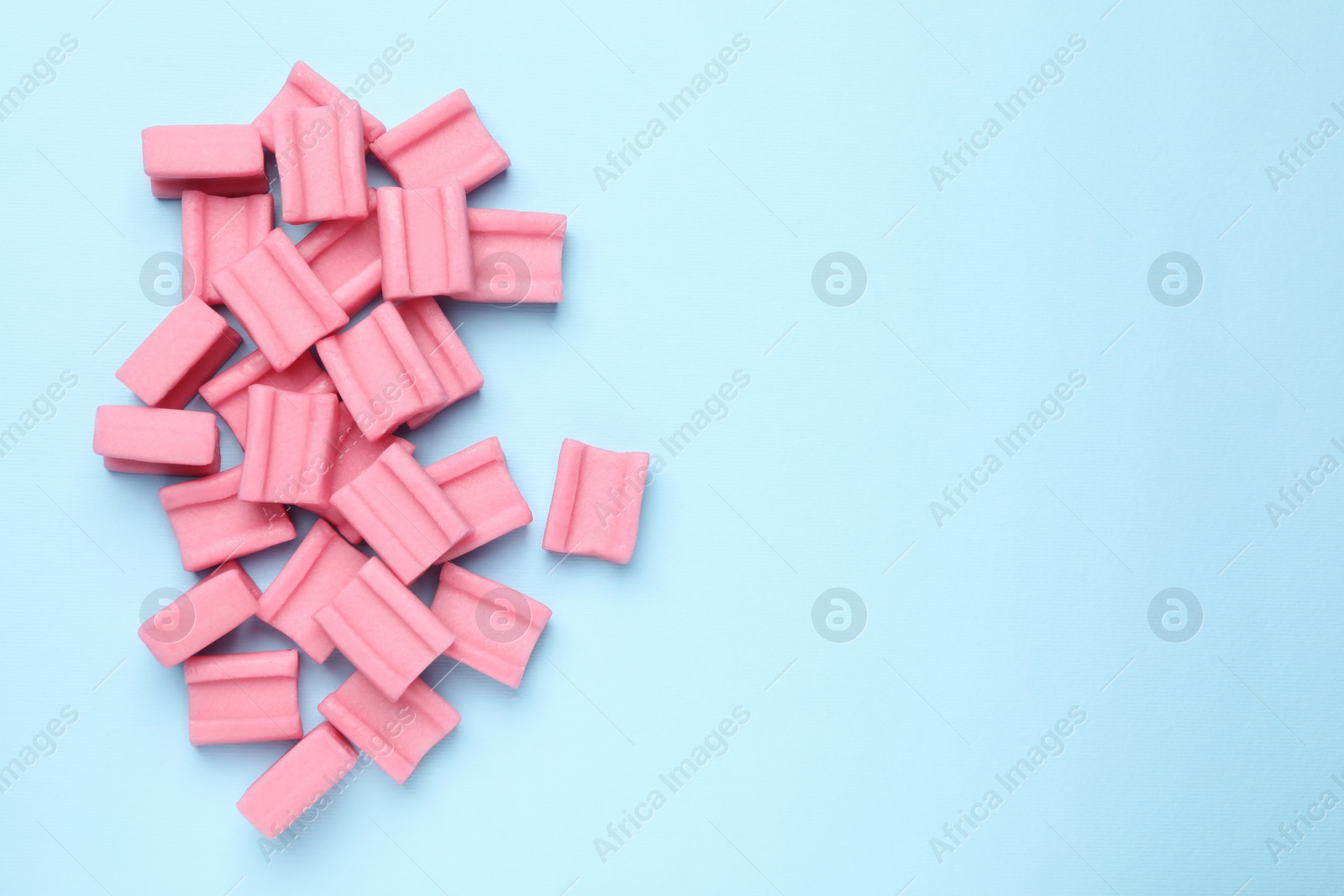 Photo of Tasty pink chewing gums on light blue background, flat lay. Space for text