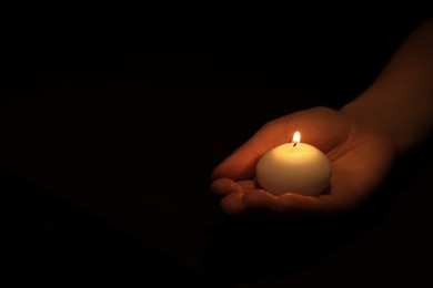 Woman holding burning candle in hand on black background, closeup. Space for text