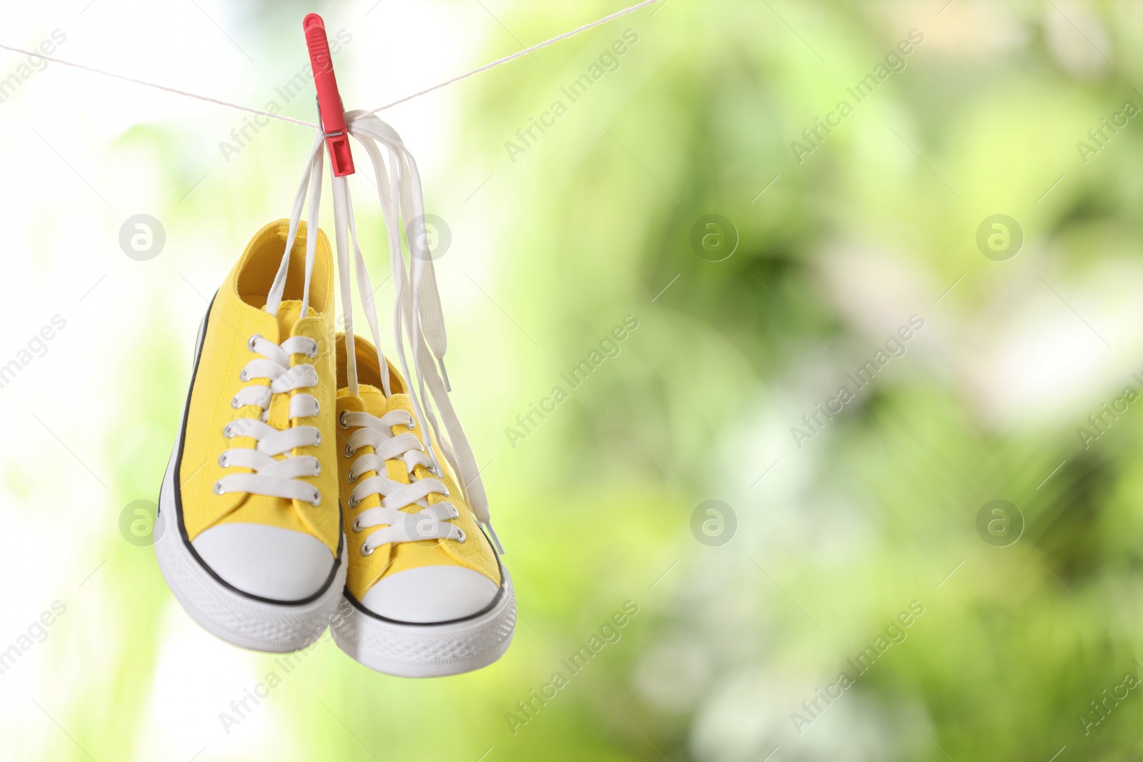 Photo of Stylish sneakers drying on washing line against blurred background, space for text