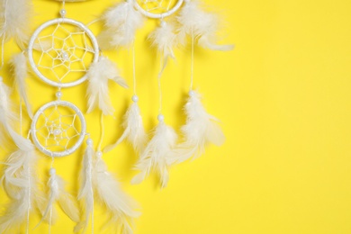 Beautiful dream catcher hanging on yellow background, closeup. Space for text