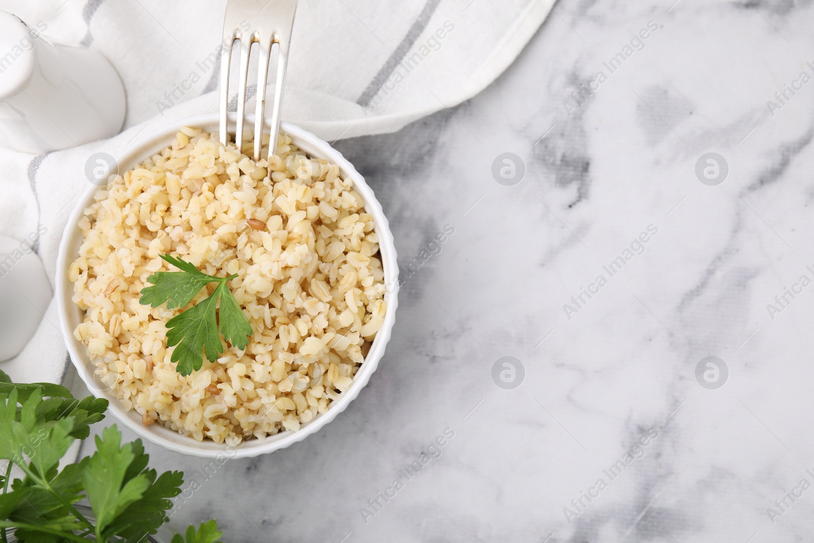 Photo of Cooked bulgur with parsley in bowl on white marble table, top view. Space for text