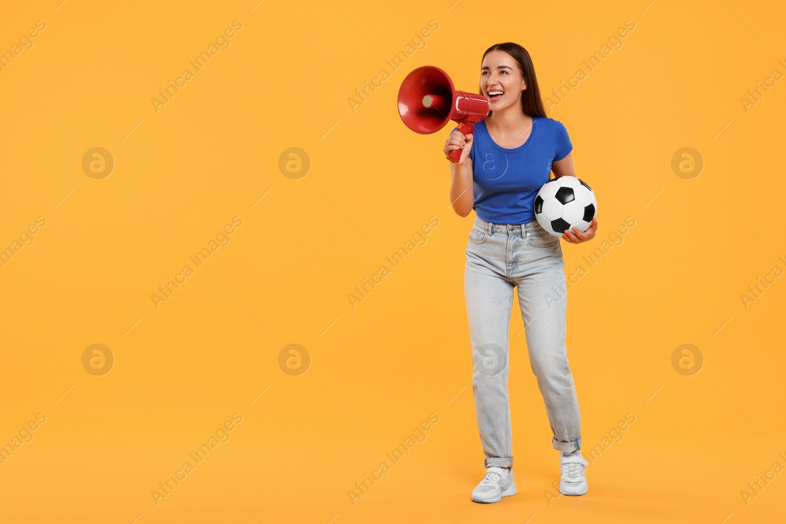 Photo of Happy fan with soccer ball using megaphone on yellow background, space for text