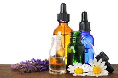 Bottles of herbal essential oils and wildflowers on wooden table, white background