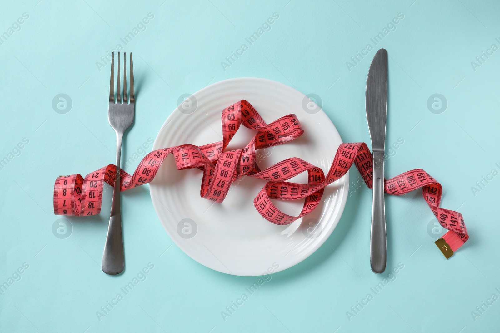 Photo of Plate, cutlery and measuring tape on light blue background, flat lay. Diet concept