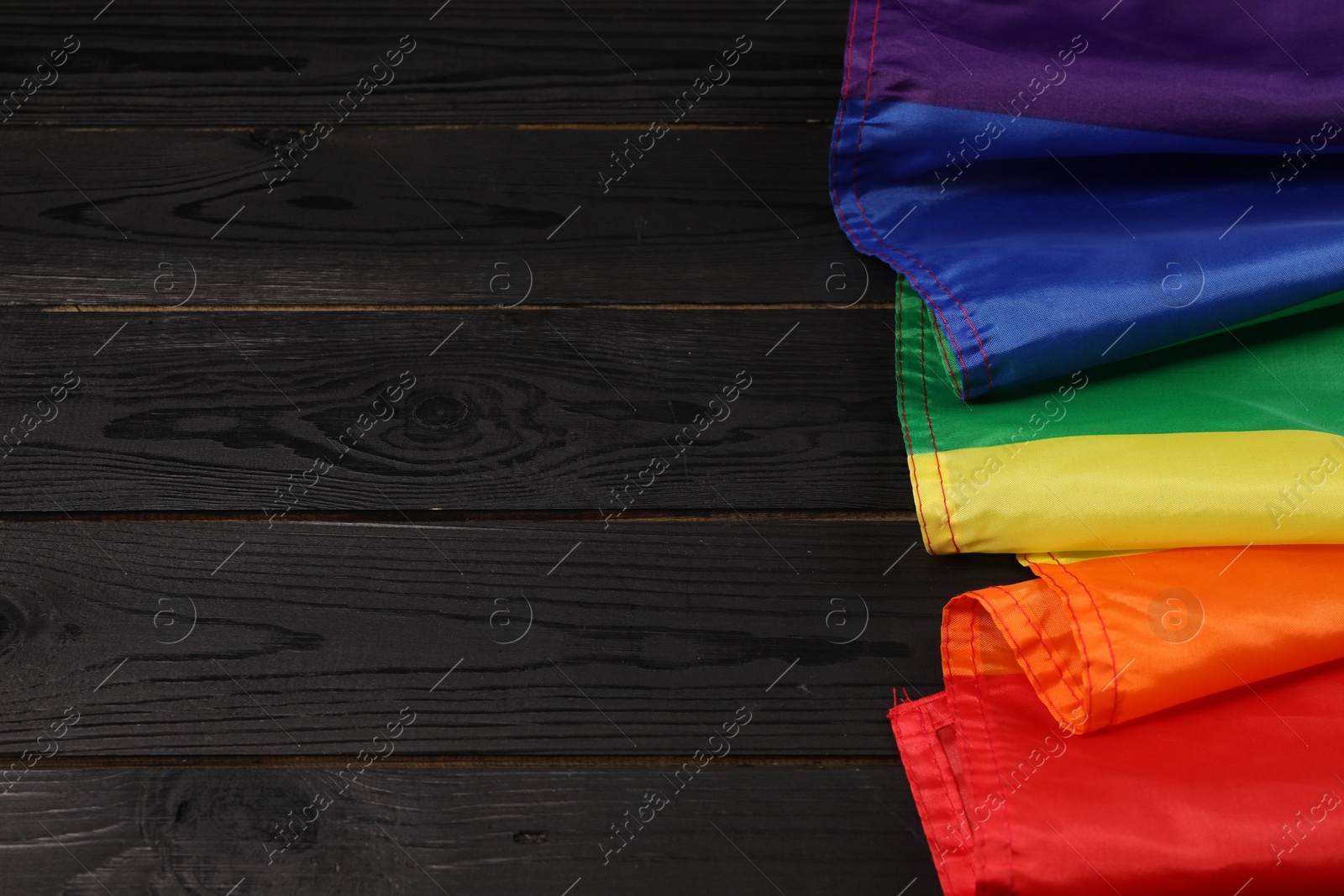 Photo of Rainbow LGBT flag on black wooden background, top view. Space for text