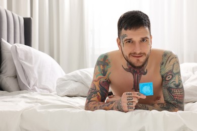 Man holding condom on bed at home, space for text